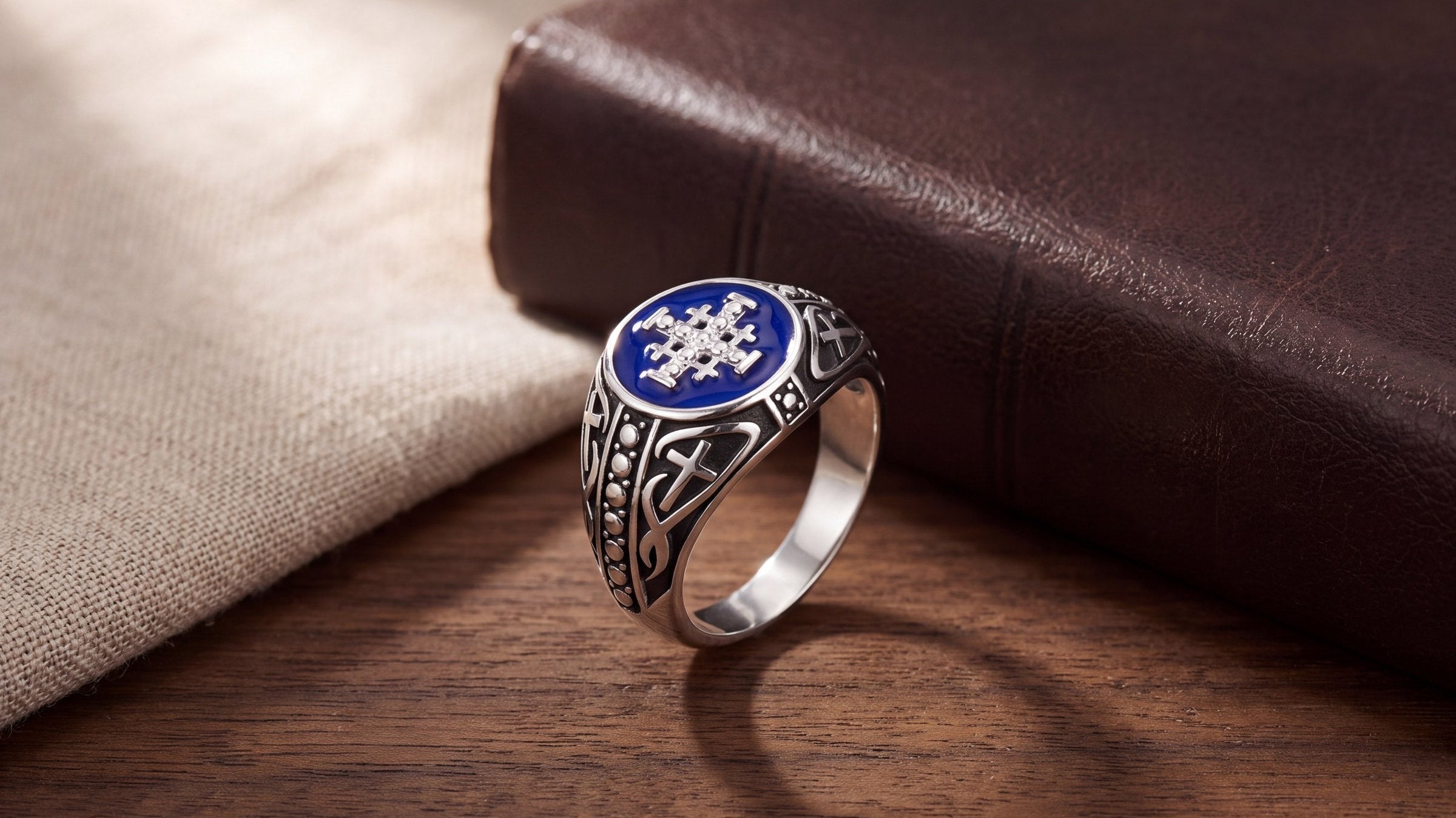Men's Jerusalem Cross signet ring with blue enamel on a walnut table beside a leather-bound book