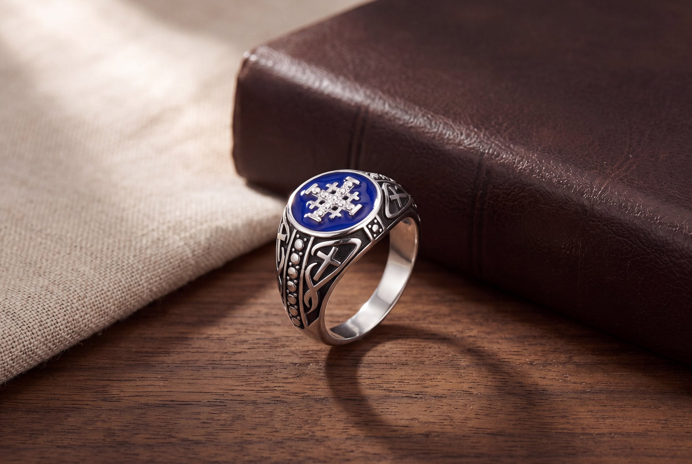 Men's Jerusalem Cross signet ring with blue enamel on a walnut table beside a leather-bound book